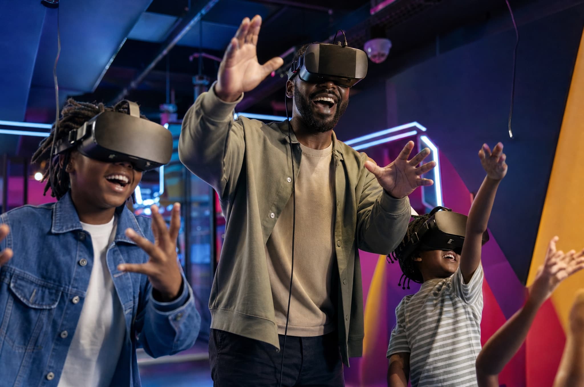 A family wearing VR headsets together in a colorful arcade, arms raised mid-game
