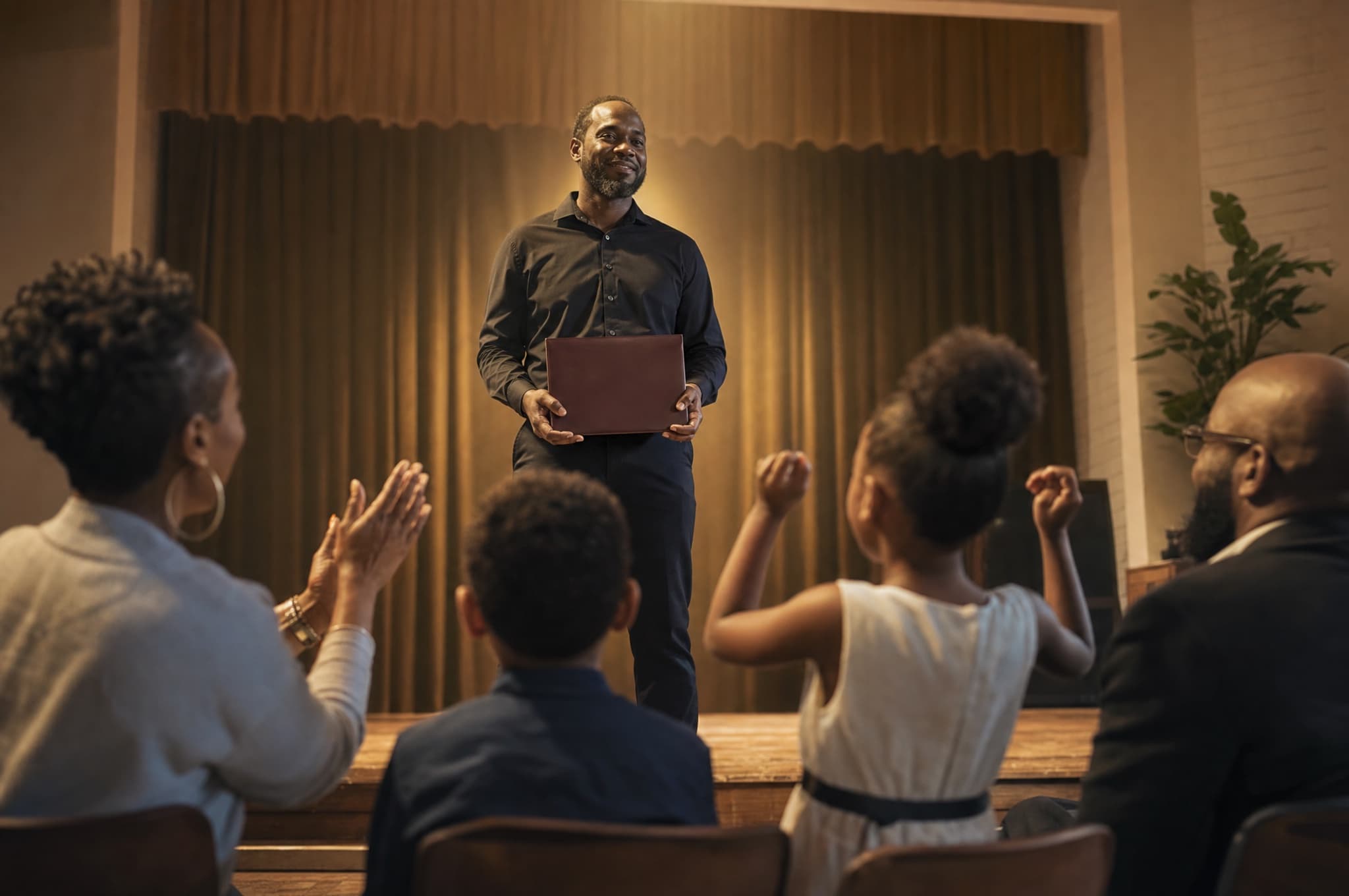 A father holding his certificate on graduation day while his kids and family cheer from the front row
